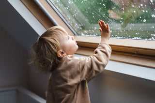 Little boy standing next to window or skylight with his hands on it as snow is covering the outside